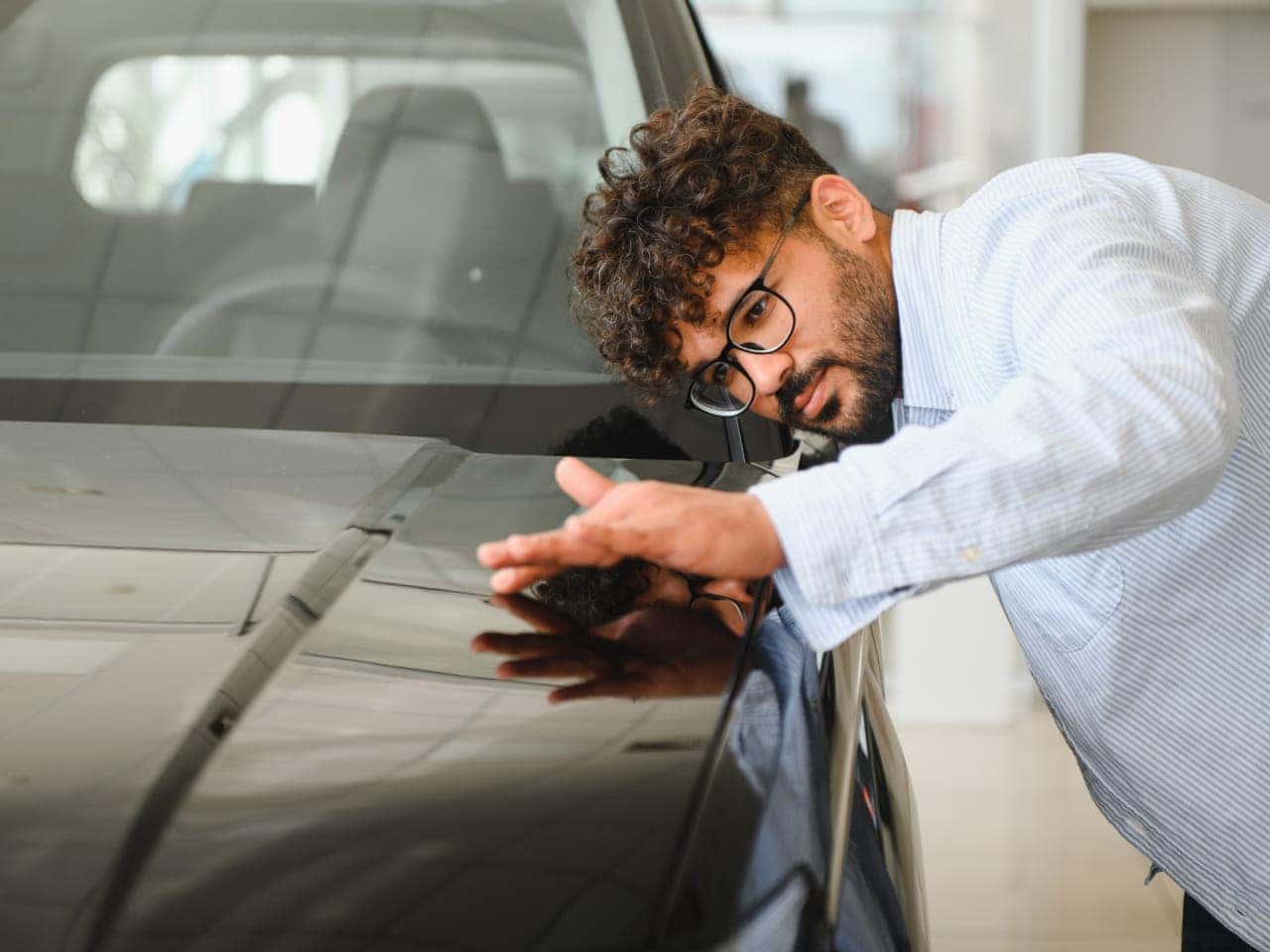 Man examines a car's glossy black surface intently.