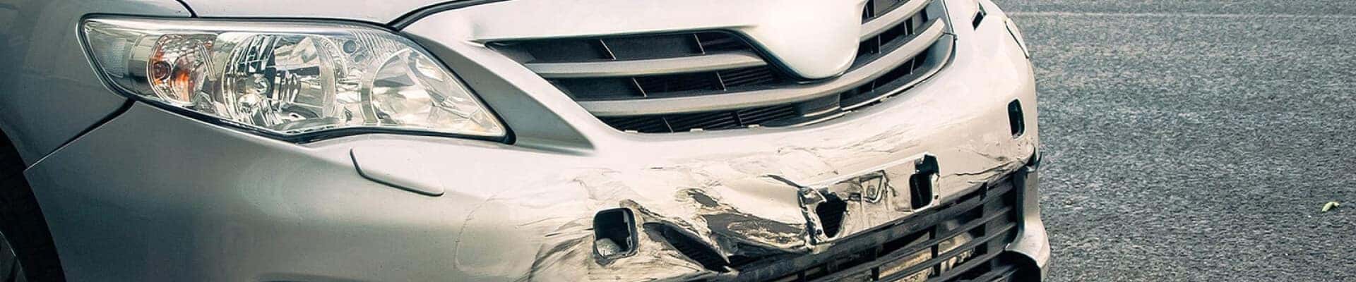 A exterior close-up of a white car with significant front bumper damage.