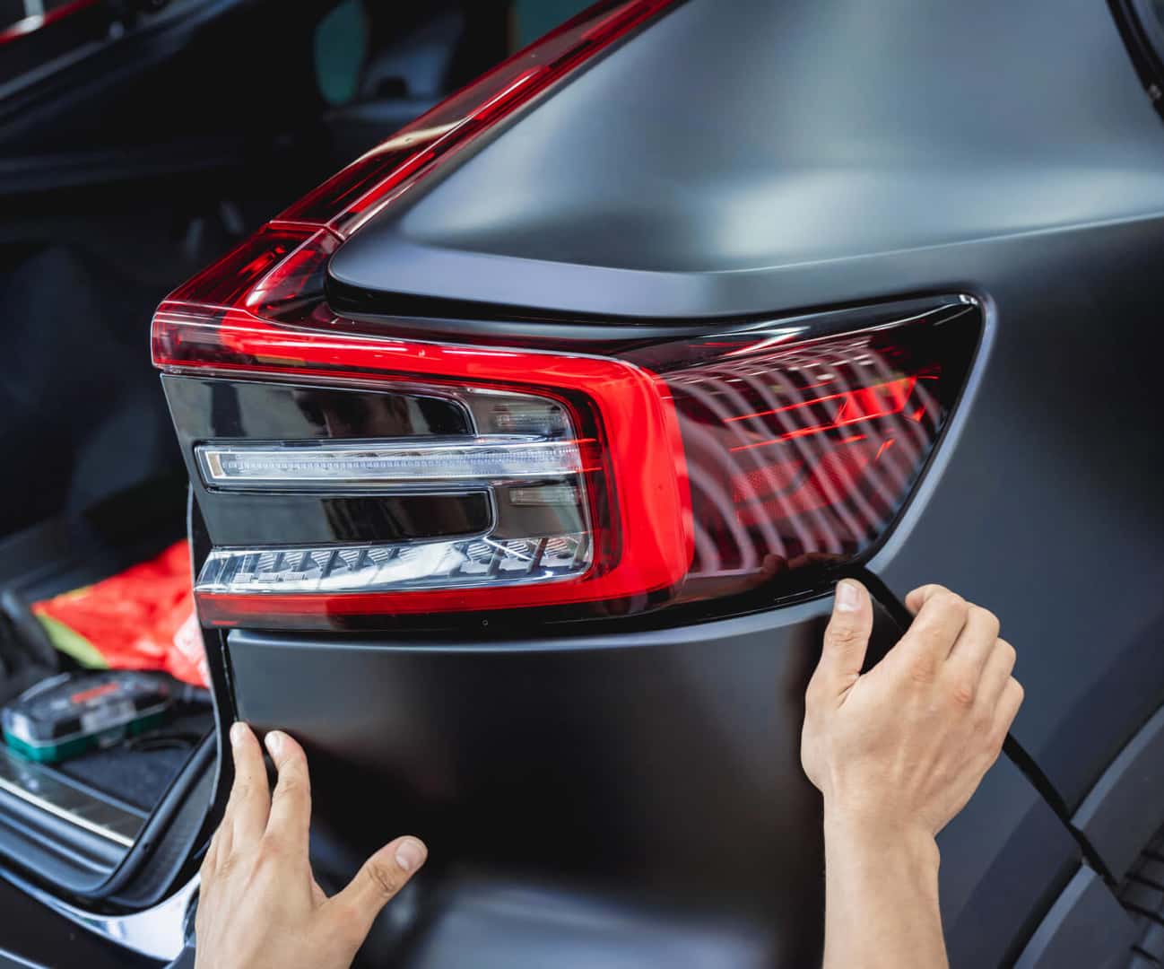 Close-up of hands aligning a replacement bumper on the rear of a car.