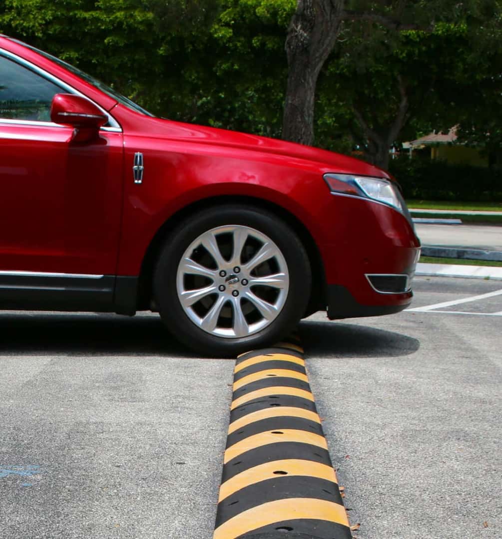 Exterior side view of a red Lincoln car driving over a speed bump.