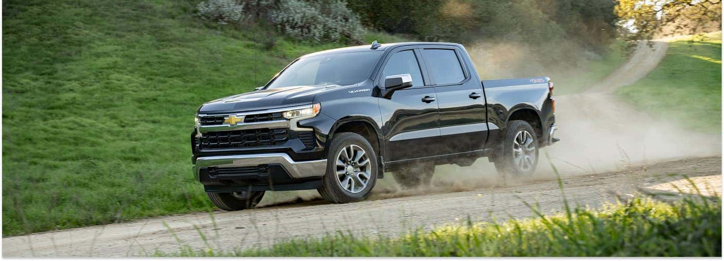 Black 2026 Chevrolet Silverado 1500 driving on a dirt road, viewed from a front three-quarter angle.