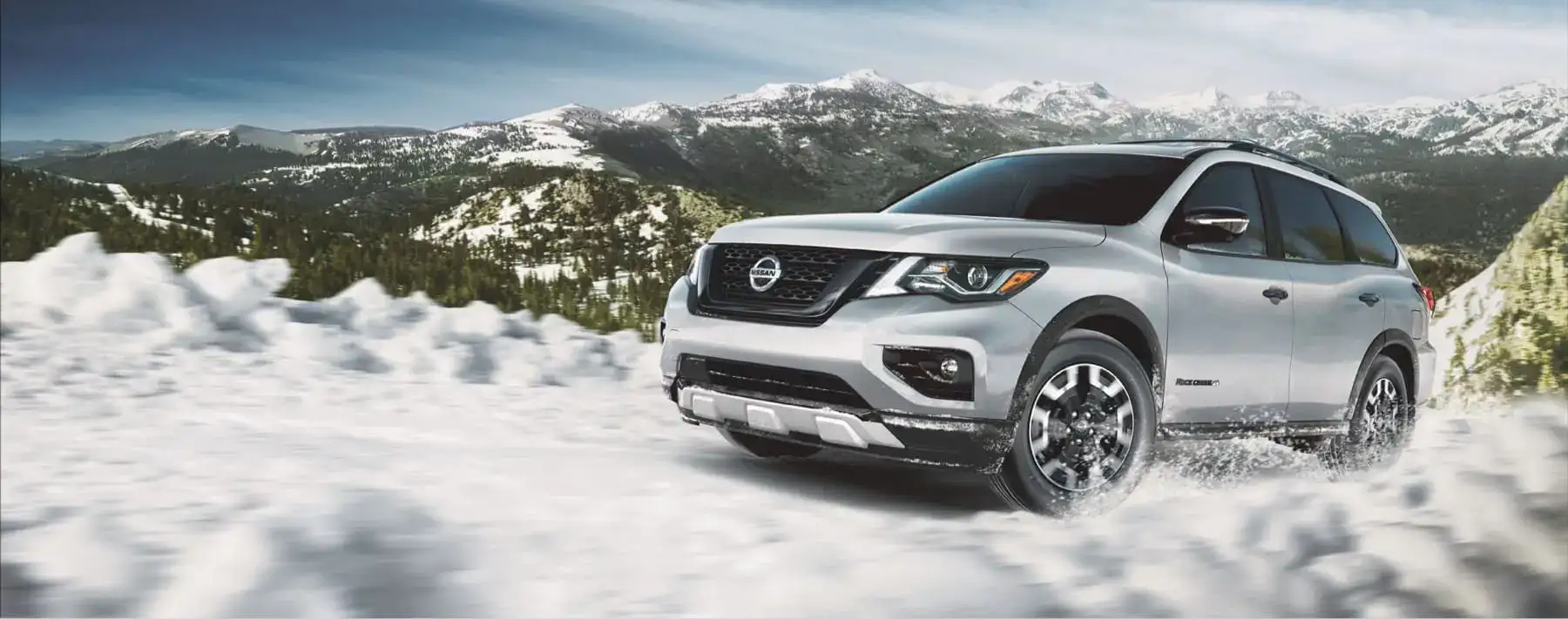 A silver Nissan SUV driving through a snowy mountain road.